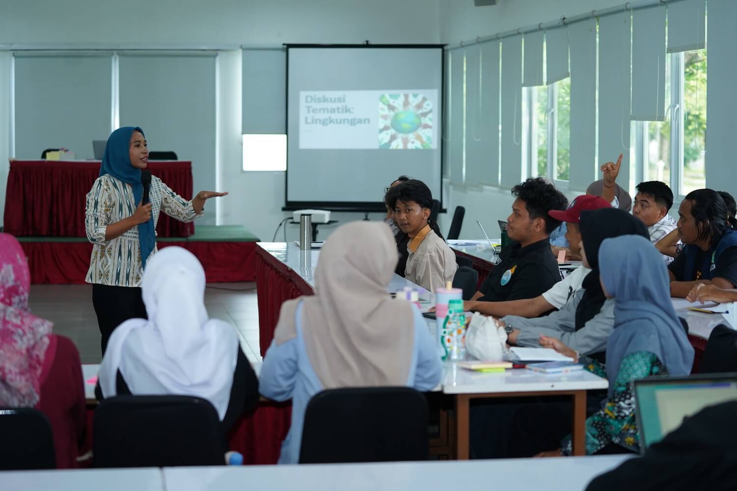 A female facilitator leads an interactive thematic discussion on environmental issues with young participants.