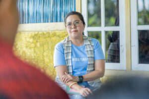 Ivony Tallo, A woman wearing glasses, a light blue T-shirt with “#BETAU” printed on it, and a checked scarf sits with her arms crossed during a discussion, talked about how members have learned how to navigate public services, respond to cases of violence, and explore livelihood opportunities.