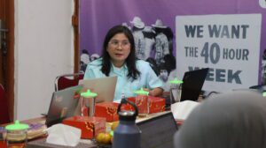 Nina Hendarwati, INKLUSI Safeguarding Focal Point, with long black hair and glasses, sits at a meeting table with a laptop during a safeguarding discussion.